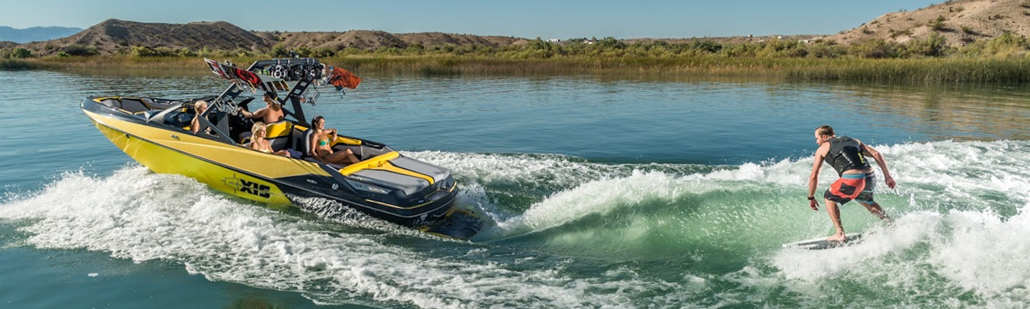 Four people on a 2020 Axis Wake Research boat pulling someone on a wakeboard in a lake.